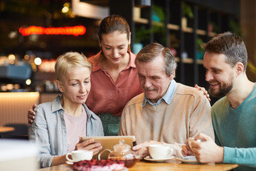 Family with adult children watching photos on tablet pc together while having lunch in cafe