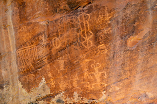 A petroglyph panel featuring patterened body anthropomorphs with antenna on their heads that look like rabbit ear men below a calendar and blanket pattern.