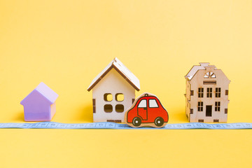 several models of houses on a yellow background, measured blue tape for measuring distance, red car toy, social distance during quarantine, stay at home concept, copy space