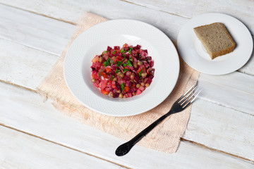 Vinegret beetroot salad  in  plate on table cloth with fork and bread on white wooden background