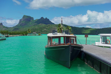 Wooden Boat and Dock in Turquoise Lagoon Waters in Foreground with Volcanic Mountain Island in Background in Bora Bora French Polynesia