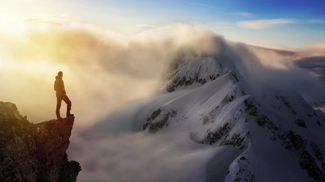 Cinemagraph Continuous Loop Animation. Fantasy Adventure Composite with a Man on top of a Mountain Cliff with Dramatic Landscape in Background during Sunset or Sunrise. Landscape from BC, Canada.