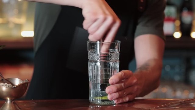 the process of making lime, mint and ice cocktail, mix the cocktail with a spoon. Close up of an experienced bartender who makes Mojito cocktails with lime, mint