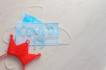Composition with disposable face mask, decorative crown and sign "COVID-19"on color background