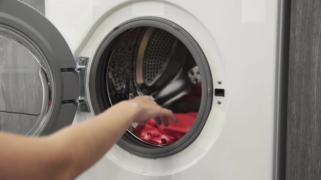 Female hand puts COLORED CLOTHES in laundry machine. Loading washing machine. Load clothes to washer machine. Load clothes laundry washing machine. Preparing laundry washing