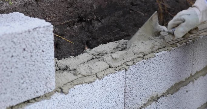 bricklayer building wall from ceramsite concrete blocks, applying mortar with trowel