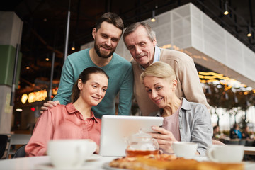 Family of four talking to their relatives online using digital tablet during their lunch in cafe