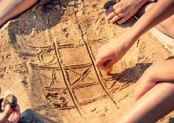 tic tac toe game or X O game write on sand. Fun and games on the sandy beach. Children's hand draws a shell on the sand