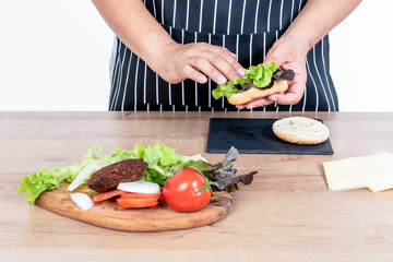The butler is cooking a hamburger Which contains fres vegetables, meat and sheese, Is a food that is easy to make And nutritious, On white background to people and food concept.