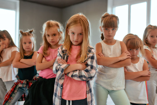 Modern dancers. Group of confident little girls keeping arms crossed, making serious faces and looking at camera while standing in the dance studio