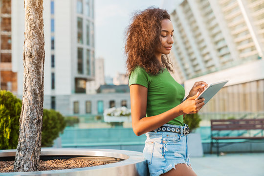 Young Girl Using Digital Tablet At City Street On Sunny Summer Day