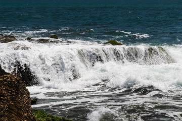 Wave cascading over rocks exposed at low tide; on the coast of Bali, Indonesia. 
