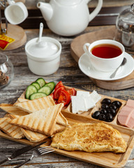 breakfast setup with omelet toast cucumber tomato cheese olive and tea