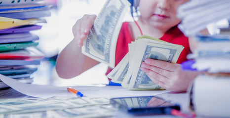 Humorous photo of cute little business child girl works in office and maks money. Selective focus on US Dollar bills.