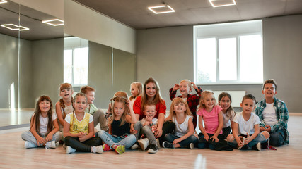 Making a photo. Group of positive little boys and girls in fashionable clothes posing with their young female teacher in the dance studio