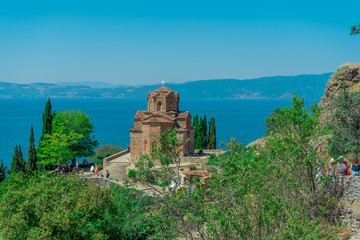 Fototapeta na wymiar Surrounded by green trees Church of St. John at Kaneo and Lake Ohrid as a background. August 2019