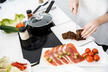 A Young Girl is Preparing a Dish With Fresh produce in a White Kitchen. Slice dark Bread on Board