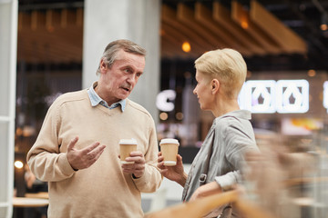 Mature couple with coffee drinks talking to each other while standing in the mall