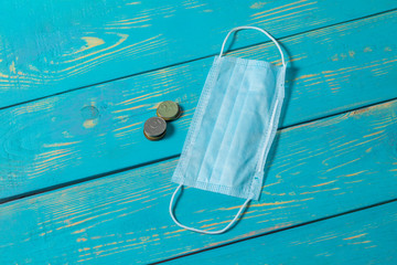Fototapeta na wymiar wooden blue background in retro style. Disposable medical face mask next to coins
