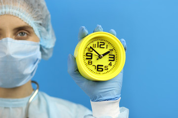 attractive woman doctor or nurse in a medical gown holds an alarm clock in her hand