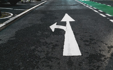 Road marking on the asphalt: white paint branch arrow pointing forward and to the left, a fragment...