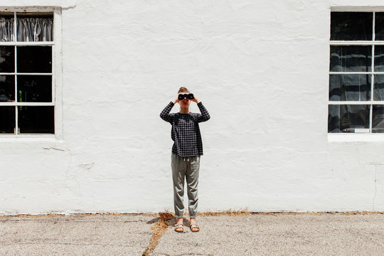 Full body of preteen girl facing the camera while looking into a pair of binoculars