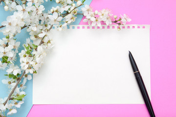 Empty sheet of notepad with pen on a pink-blue background with blossom flowers. Copy space for spring text.