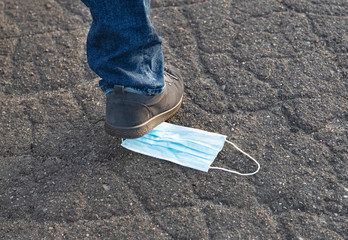 Neglect of the quarantine rules and personal protective equipment necessary in connection with the outbreak of the pandemic disease COVID-19, SARS-COV-2 disease. A person steps on a mask.