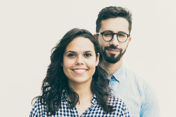Positive guy in casual standing behind his beautiful girlfriend. Young woman in casual and man in glasses in glasses posing isolated over white background. Happy couple portrait concept