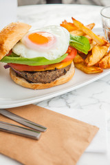 Burger with French fries on white table, with vegetables.