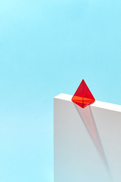 Red plastic pyramid on white box with shadow around blue background with copy space.