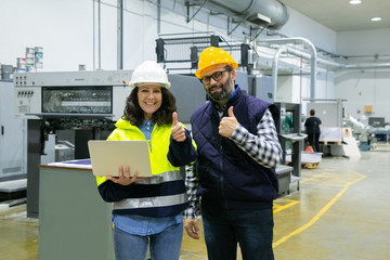 Happy positive engineers with laptop computer showing like gesture at camera. Middle aged man and...