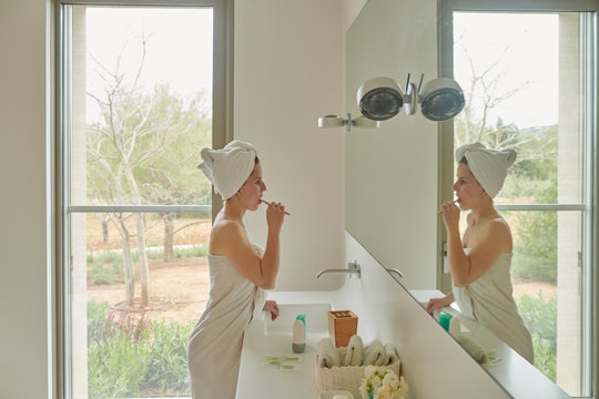 Female after shower brushing teeth in bathroom.