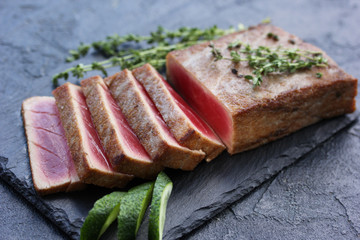 Fried tuna with thyme and fresh cucumber on a black board on a black background. Seafood. Background image, copy space