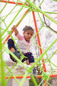 Young child with braids in her hair climbing a spider string type structure at a playground