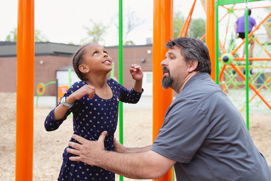 Portrait of a father helping his daughter jump and hold onto the monkey bars at the playground