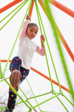 Young child with braids in her hair climbing a spider string type structure at a playground