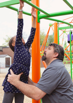 Portrait of a father helping his daughter jump and hold onto the monkey bars at the playground