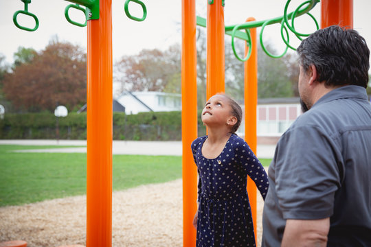 Portrait of a father helping his daughter jump and hold onto the monkey bars at the playground