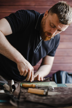 Young craftsman with beard makes a product in his workplace. Handmade.