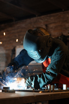 Man welding metal parts in workshop