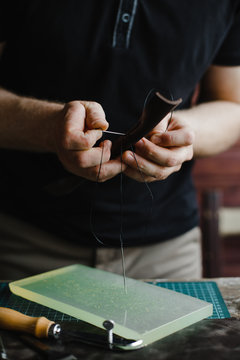 Craftsman sews a leather, using a thick needle. Photo of a creativity person