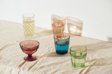 Set of colored glassware on red table over white wall.