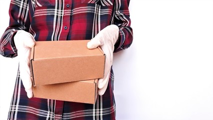 Courier in a checkered burgundy shirt with medical latex gloves safely delivers online purchases in brown cardboard boxes to the door on a white background during the coronavirus epidemic,COVID-19.