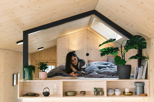 Caucasian Woman Reading on Bed of Stylish Natural Tiny House