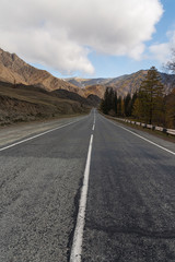 Road in the autumn mountains. Altai, Siberia, Russia. Yellow autumn forest and mountains with clouds.