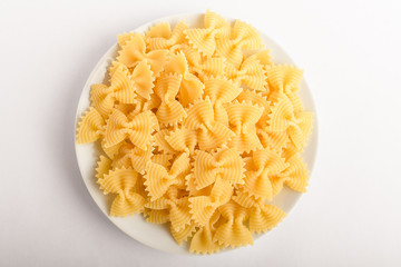 Dried Farfalle Rigate traditional Italian pasta on a plate ready to be cooked, isolated on a white table, top view or flat lay of healthy food 
