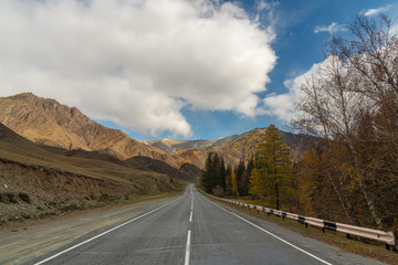 Road in the autumn mountains. Altai, Siberia, Russia. Yellow autumn forest and mountains with clouds.