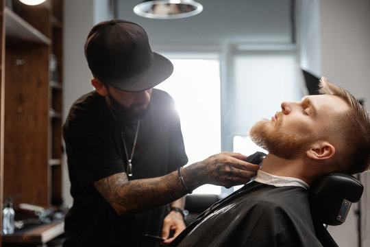 Man shaving beard of client in salon chair