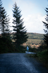 Back view of a young woman hiking in Irish forest. Hiking girl is walking in gloomy mystical and dark forest - thriller scene. Wide-angle lens, selective focus.